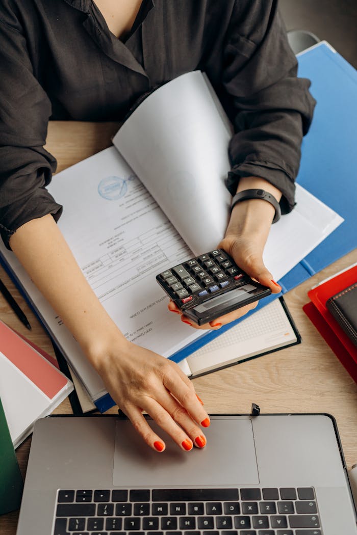 Home A business professional uses a calculator among documents and laptop on a desk for financial tasks.