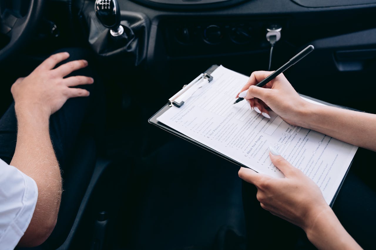 Home Close-up of a person writing on a clipboard inside a car, showing hands and a gear shift.